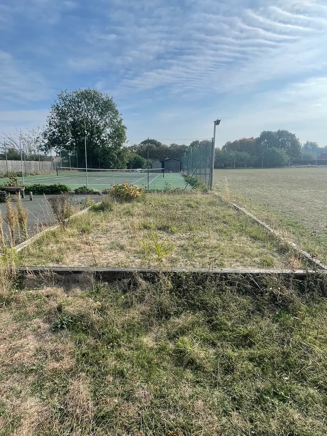 The disused pétanque piste in Wetherden — a timber-edged rectangle overgrown with grass and weeds, beside the tennis court and playing field.