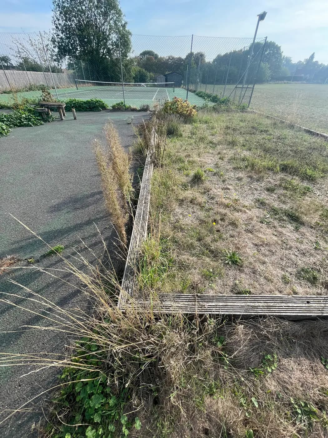 The disused pétanque piste in Wetherden — a timber-edged rectangle overgrown with grass and weeds, beside the tennis court and playing field.