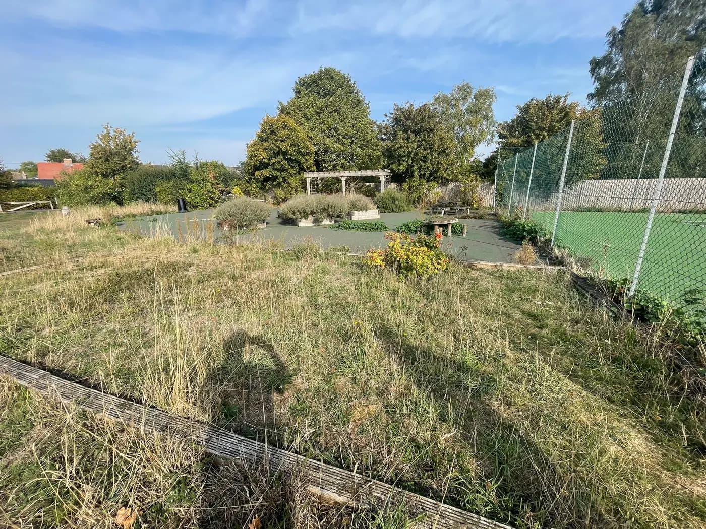 The disused pétanque piste in Wetherden — a timber-edged rectangle overgrown with grass and weeds, beside the tennis court and playing field.